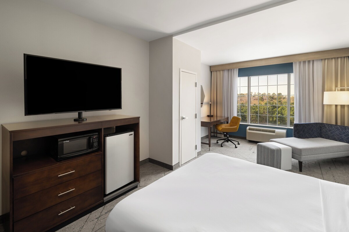 A hotel room with a bed, a TV, a desk with a chair, and a window with curtains.