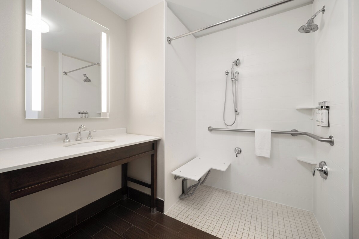 A modern bathroom with a large mirror, a sink, and a walk-in shower with grab bars and a handheld showerhead.