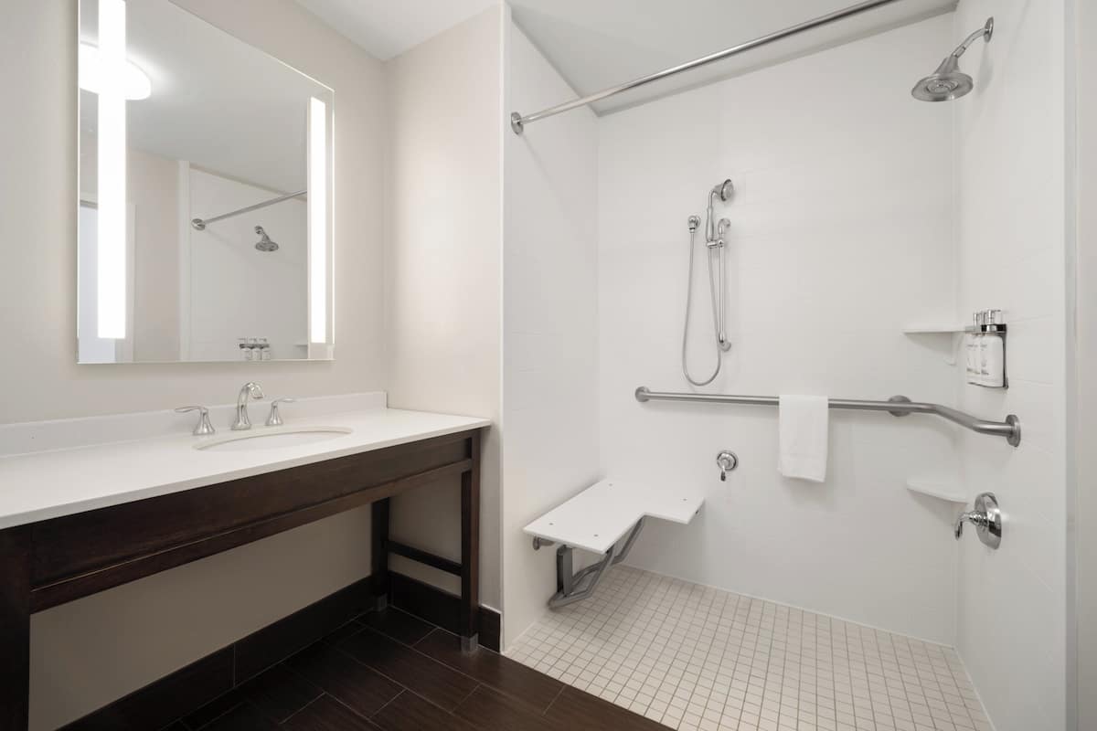 A modern bathroom with a large mirror, a sink, and a walk-in shower with grab bars and a handheld showerhead.