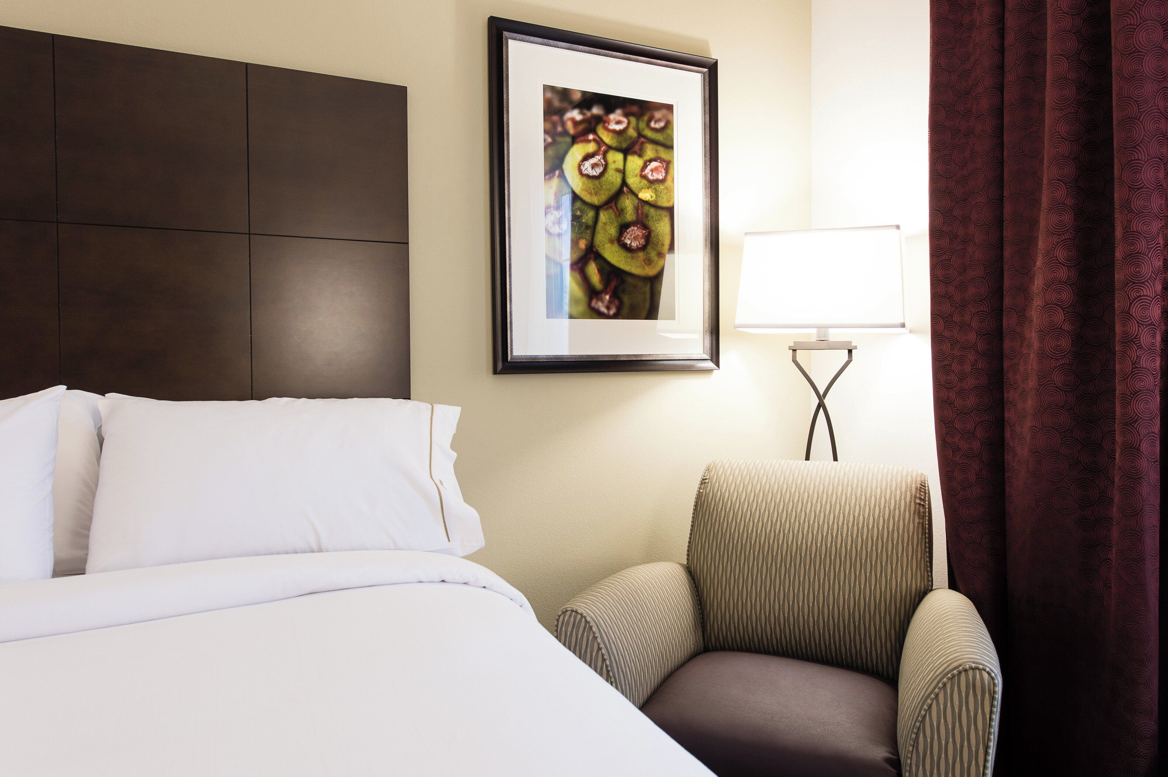 Una habitación de hotel con una cama, una silla, un cuadro en la pared y una ventana con cortinas.