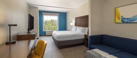 Habitación de hotel con cama, escritorio con silla, sofá, televisor y ventana con vista a árboles.