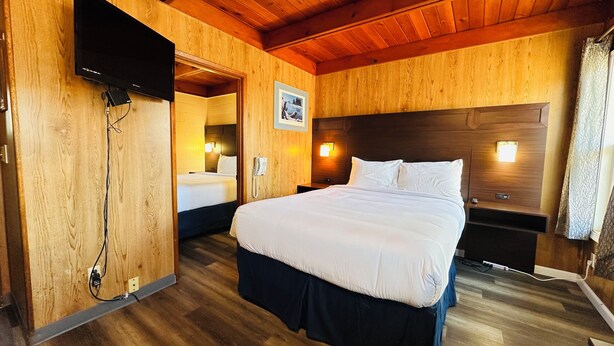 Ein Zimmer mit Holzwänden, einem großen Bett, einem an der Wand befestigten Fernseher und einem Telefon auf dem Nachttisch.
