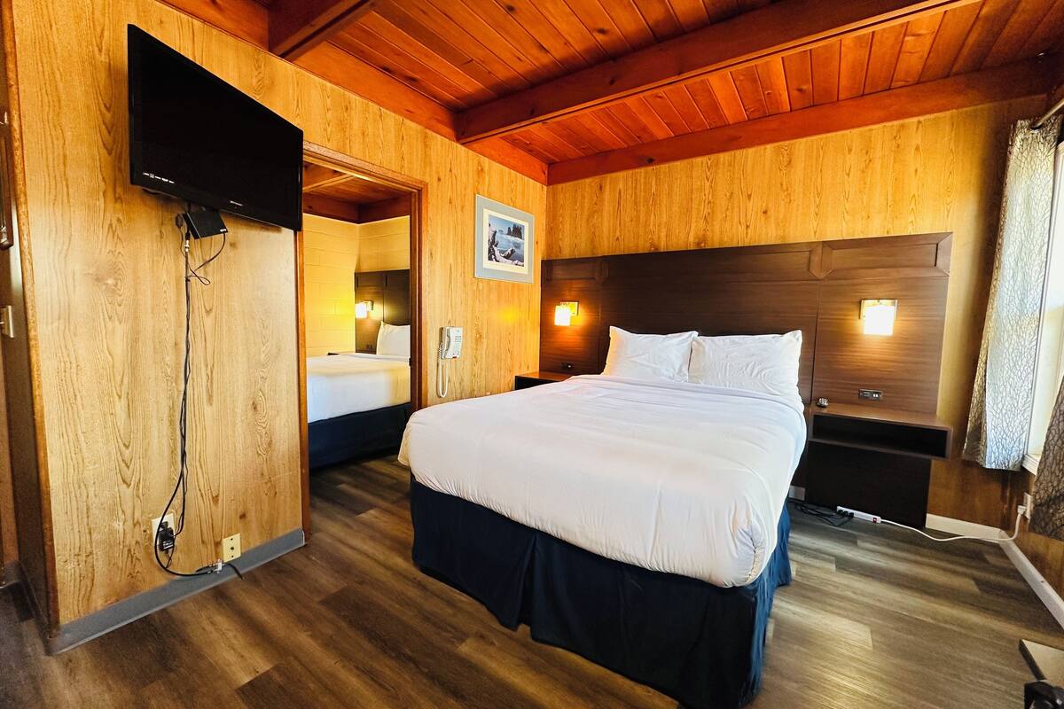 Una stanza con rivestimenti in legno, un letto grande, una TV a parete e un telefono sul comodino.