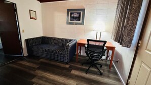 A room with a sofa, a desk, and a chair. There is a door and a window with curtains. - Anchor Inn Motel (Blaine)