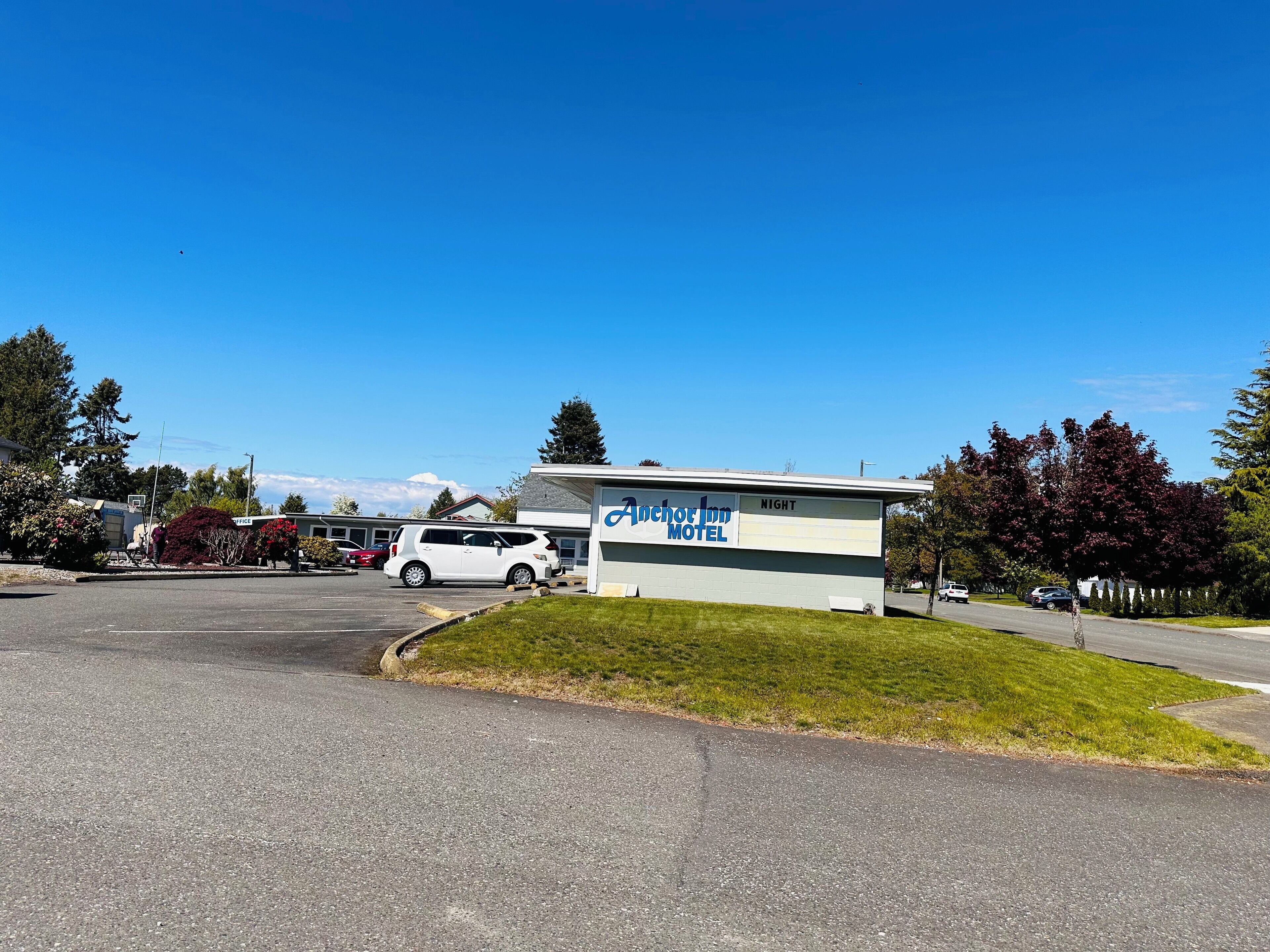Een motel met een bord waarop 'Anchor Inn Motel' staat en een parkeerplaats met meerdere auto's.