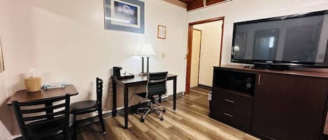 Une petite pièce bien éclairée, avec un plancher en bois, un bureau avec une chaise, une télévision et un meuble.