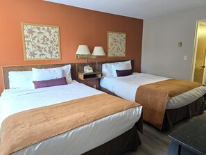 A hotel room with two beds, a nightstand with a lamp, and a telephone.