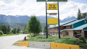 A Swiss Village Inn sign with an RV sites sign below it, set against a backdrop of mountains and a building with a green roof. - Swiss Village Inn (Golden)