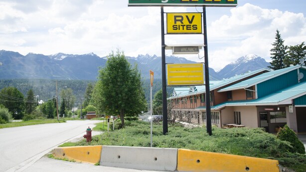 A Swiss Village Inn sign with an RV sites sign below it, set against a backdrop of mountains and a building with a green roof.