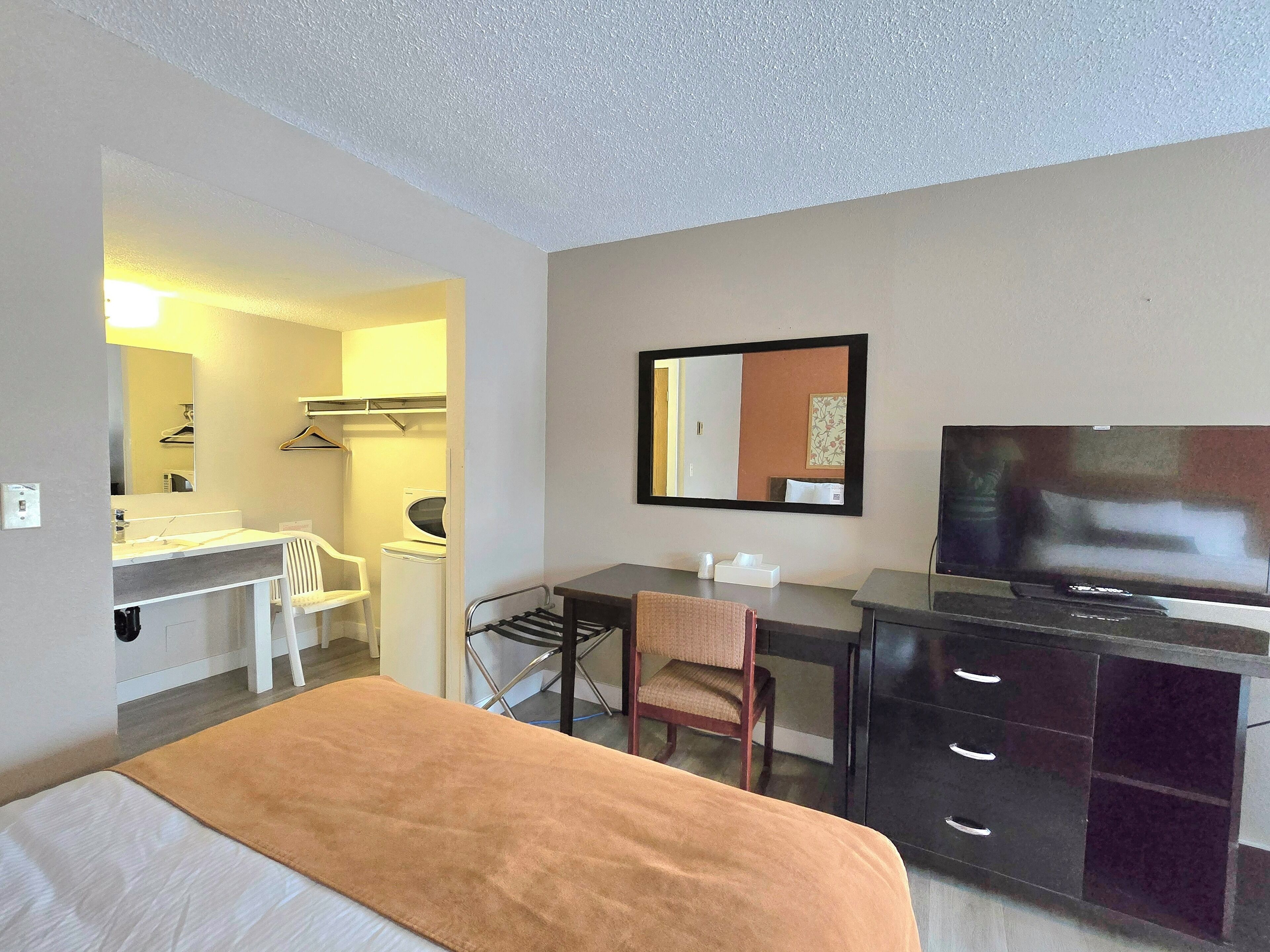 A hotel room with a bed, a desk, a chair, a TV, a mirror, a washing machine, and a drying rack.