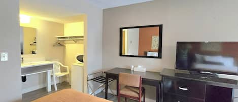 Habitación de hotel con cama, escritorio, silla, televisión, espejo, lavadora y tendedero.