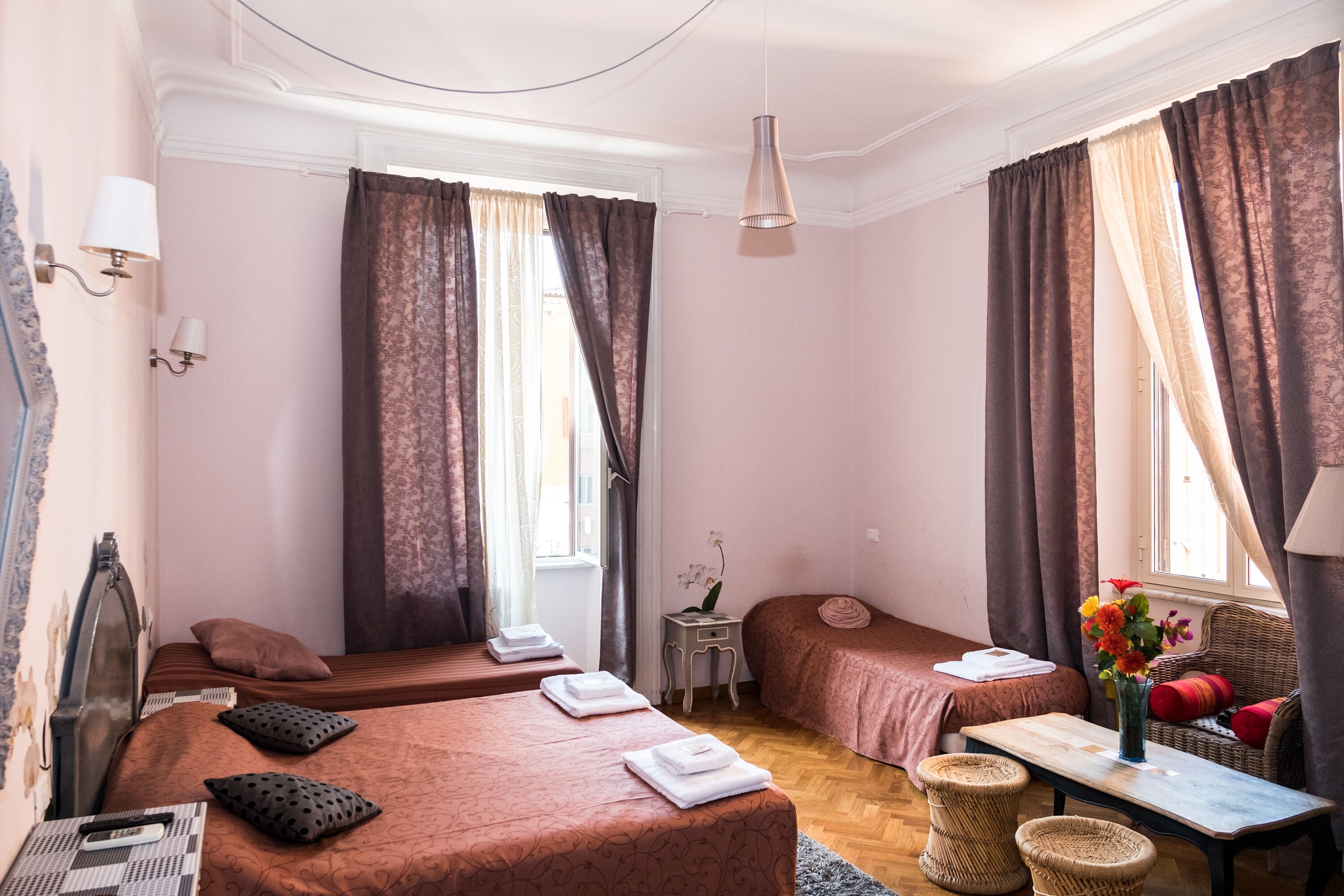 Une chambre d’hôtel avec deux lits, une petite table, une chaise et une fenêtre avec des rideaux.