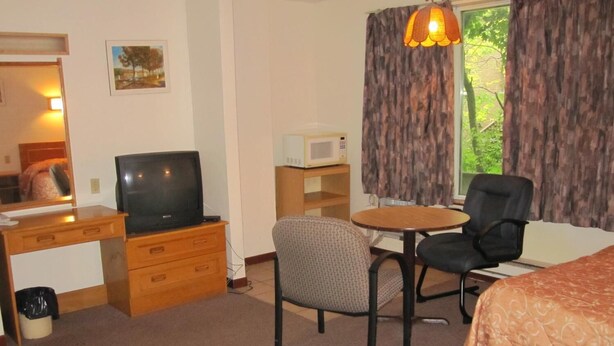 A hotel room with a bed, a desk with a television, a chair, a small table, and a microwave. - Clarkson Village Motel (Mississauga)