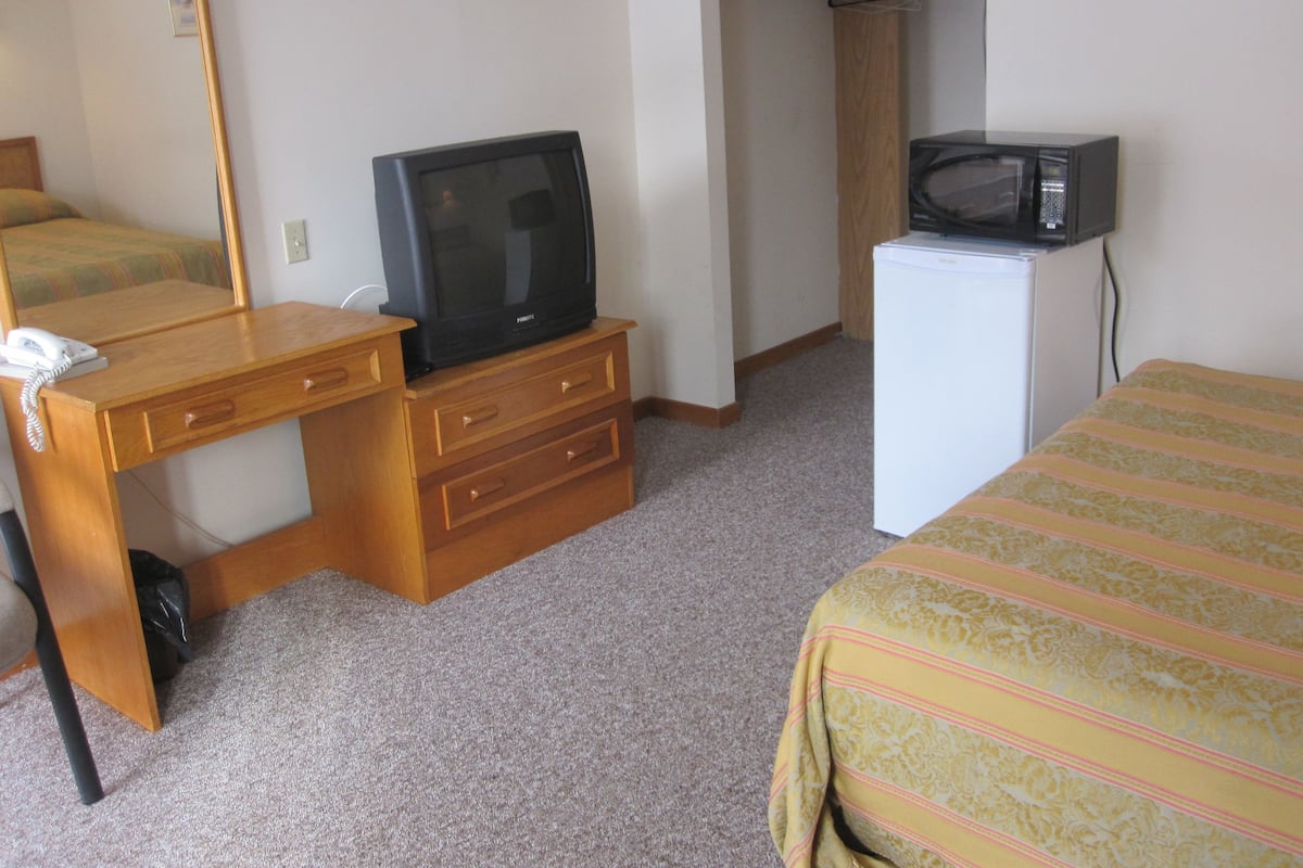 Ett hotellrum med ett skrivbord i trä, en tv, en mikrovågsugn, en säng med ett randigt överkast och en garderob.