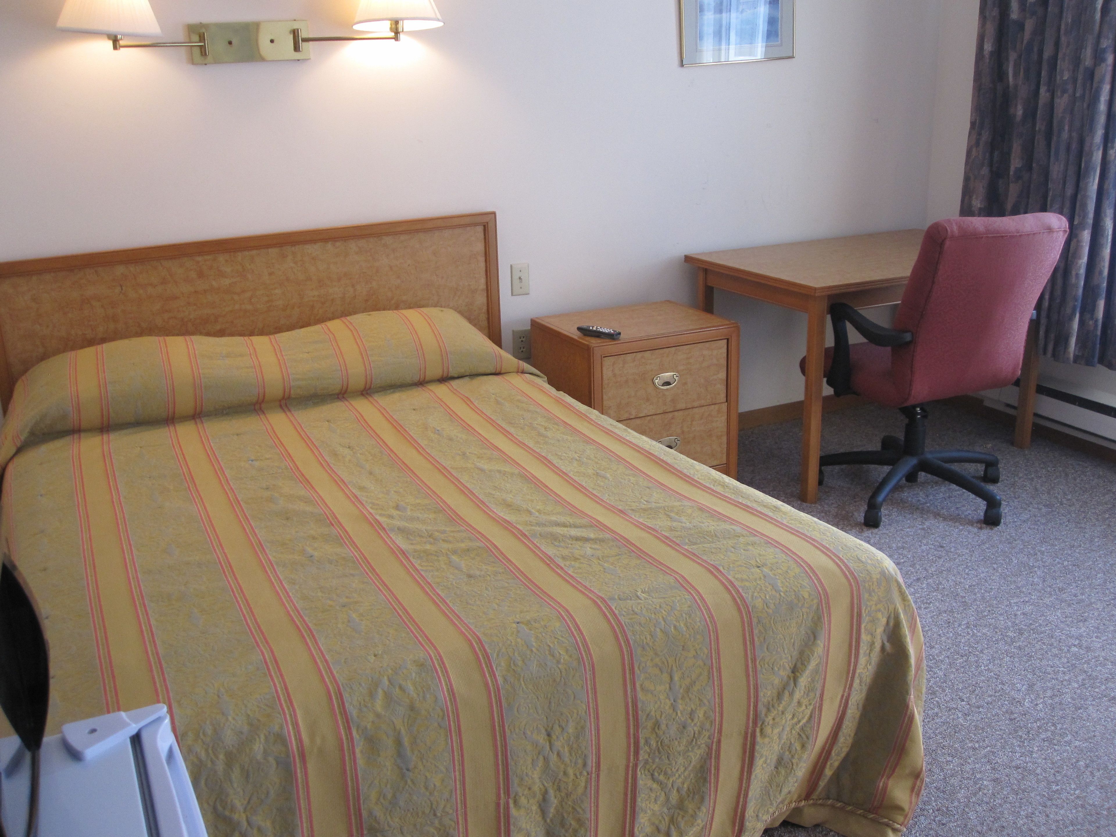 Una habitación de hotel con una cama, un escritorio, una silla y una mesita de noche.