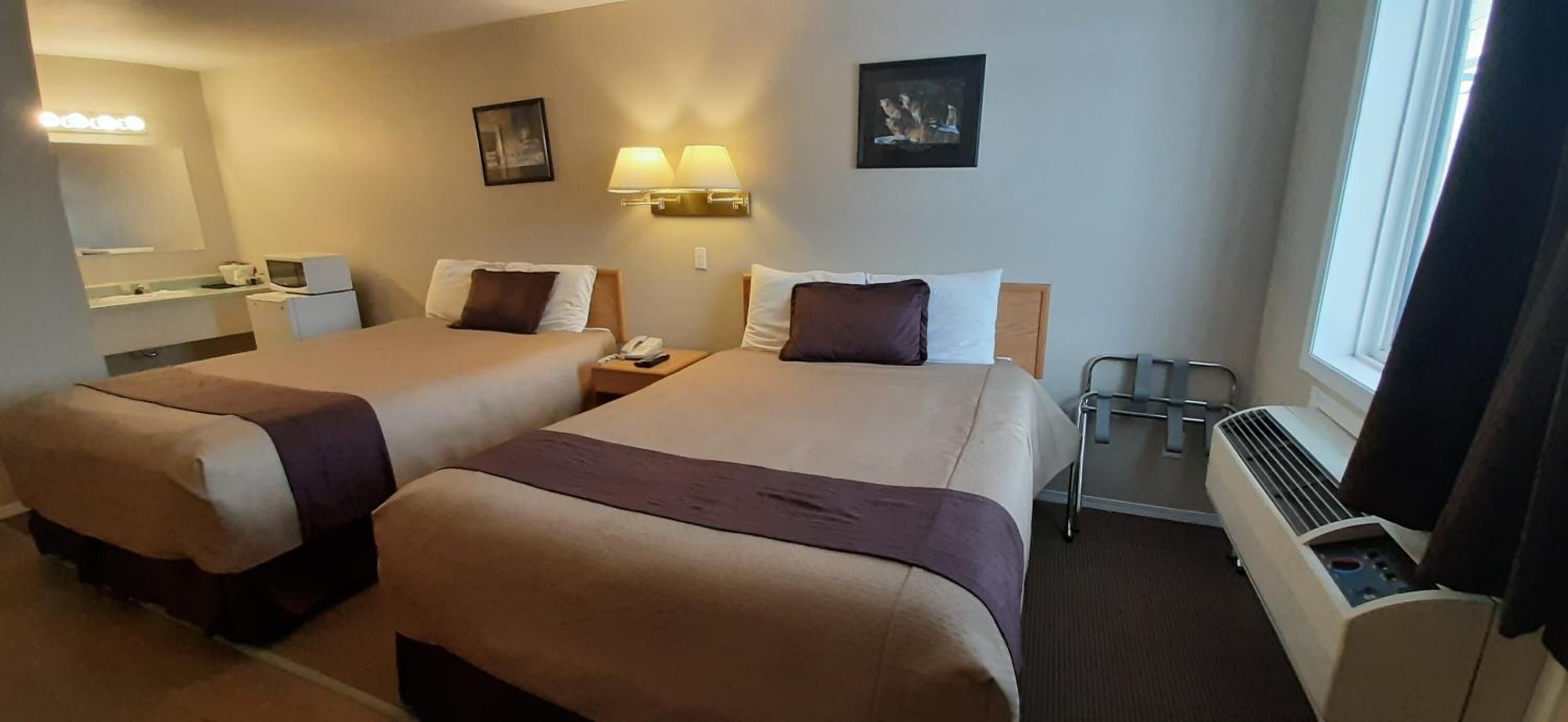 A hotel room with two beds, a desk, a chair, a heater, and a window.