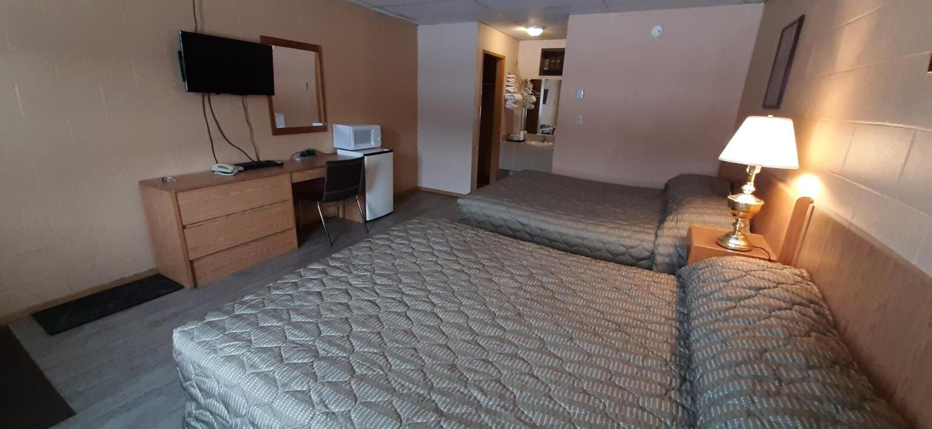 Een kleine, compacte kamer met twee bedden, een bureau met een computer en een televisie, en een lamp aan de rechterkant.