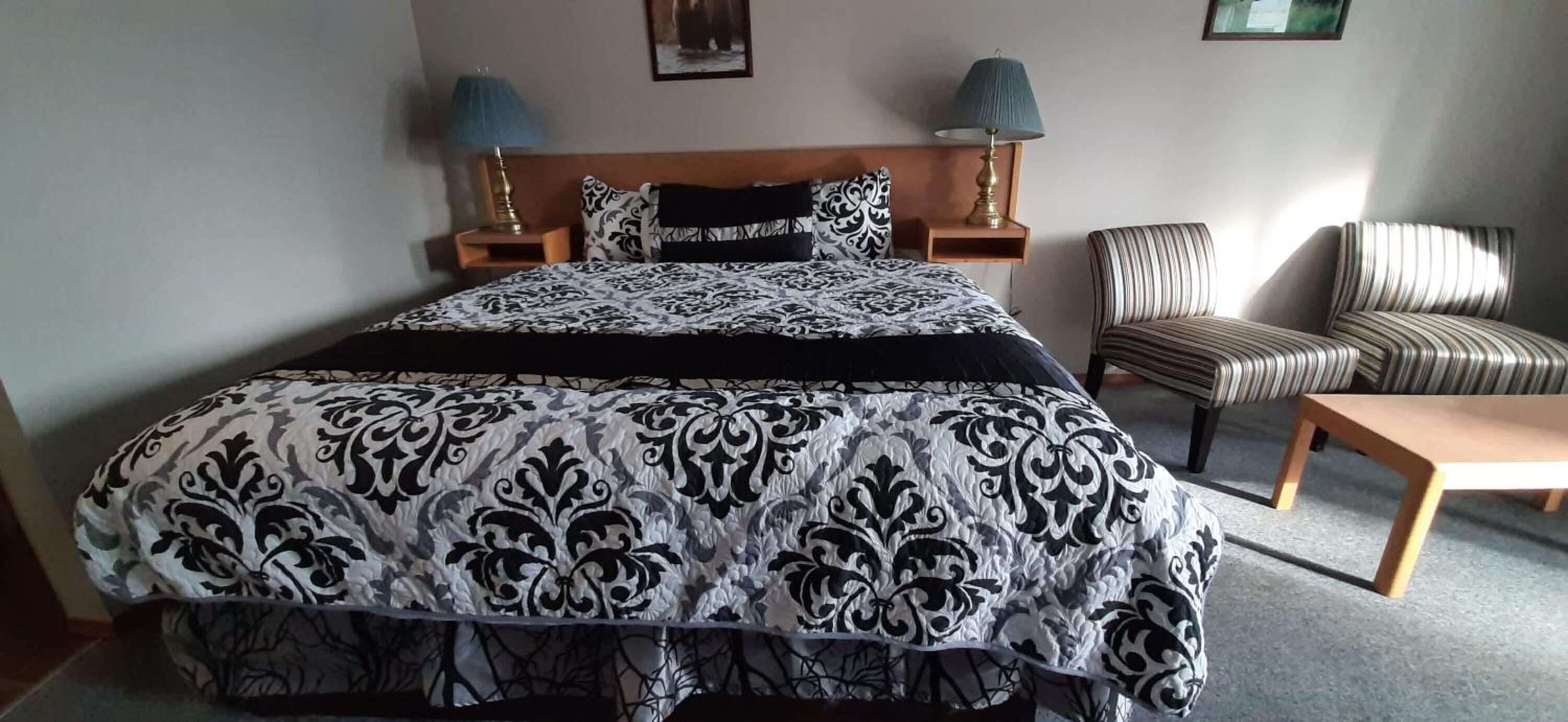 Een hotelkamer met een groot bed, twee bedlampen, een gestreept fauteuil en een houten bank.