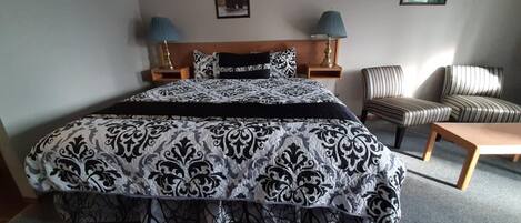 Een hotelkamer met een groot bed, twee bedlampen, een gestreept fauteuil en een houten bank.
