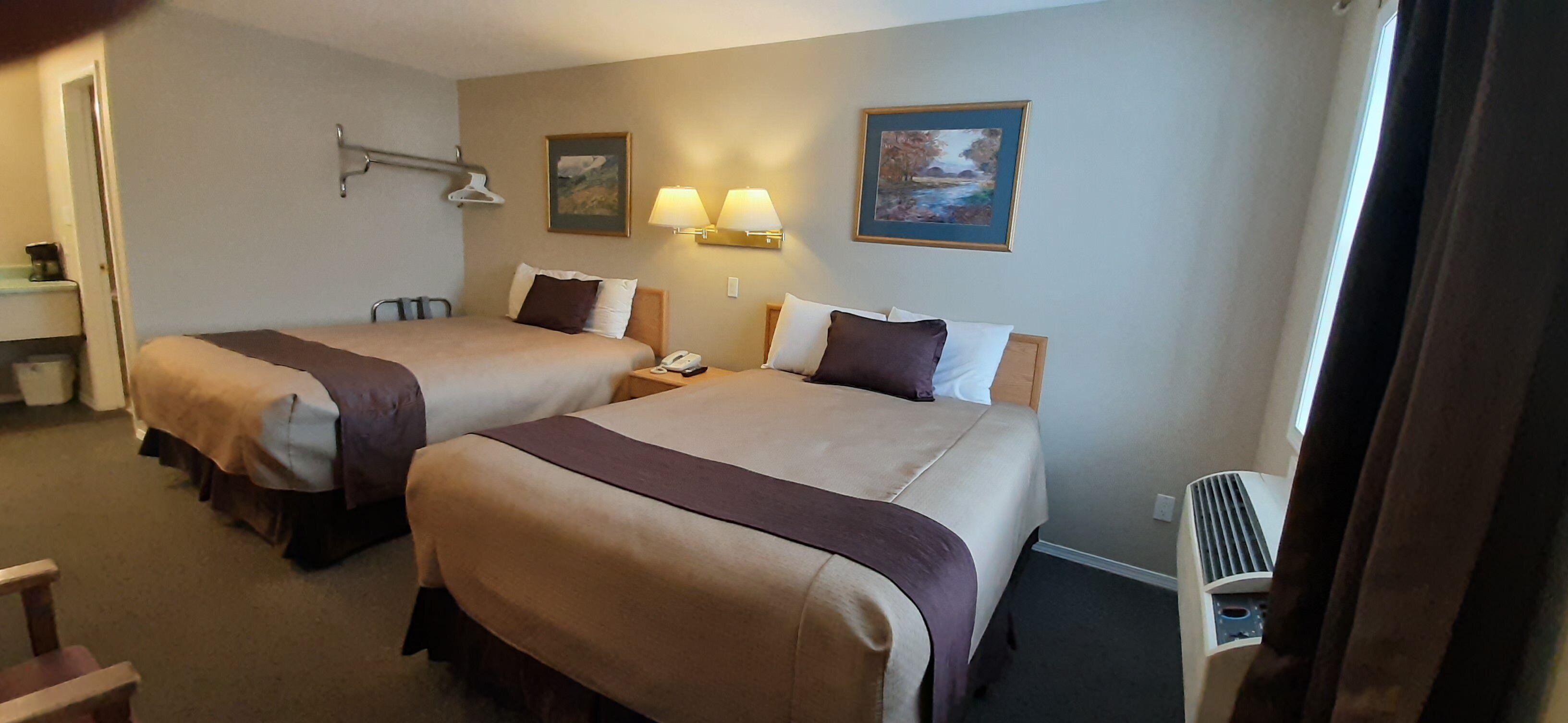 A hotel room with two beds, a desk, a chair, and a heater.