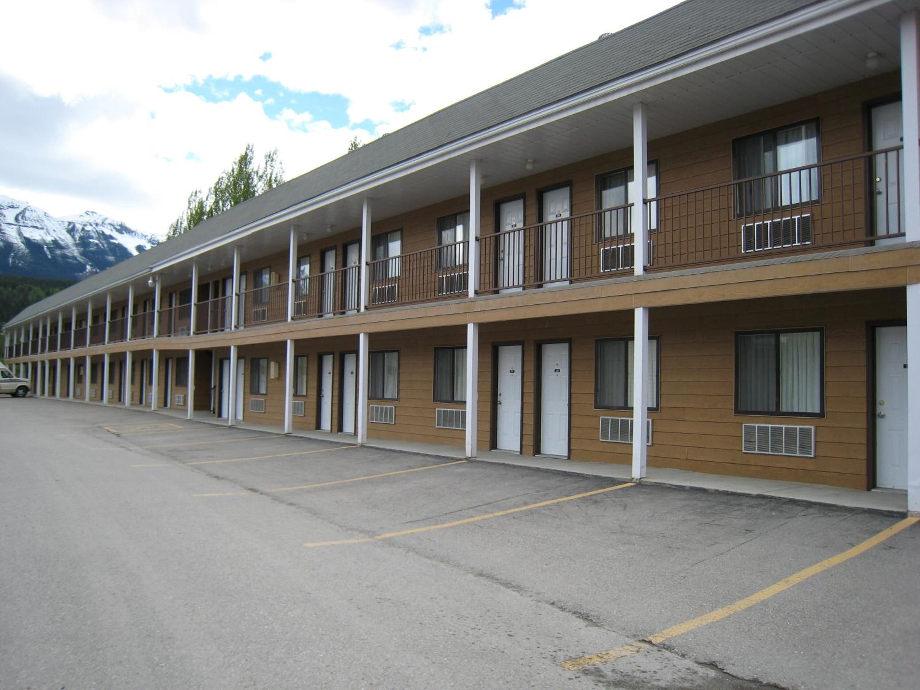 A motel with multiple rooms, a parking lot, and a mountain backdrop.