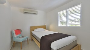 A bedroom with a bed, a chair, a window with blinds, and an air conditioning unit. - Chogogo Dive & Beach Resort Curacao (Jan Thiel)
