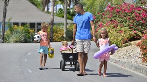 Una familia caminando por una calle, con un niño en un cochecito y otro llevando un balón de fútbol.