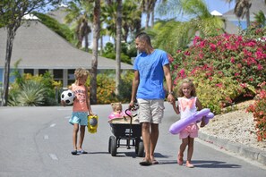 A family walking on a street with a child in a stroller and another holding a soccer ball.