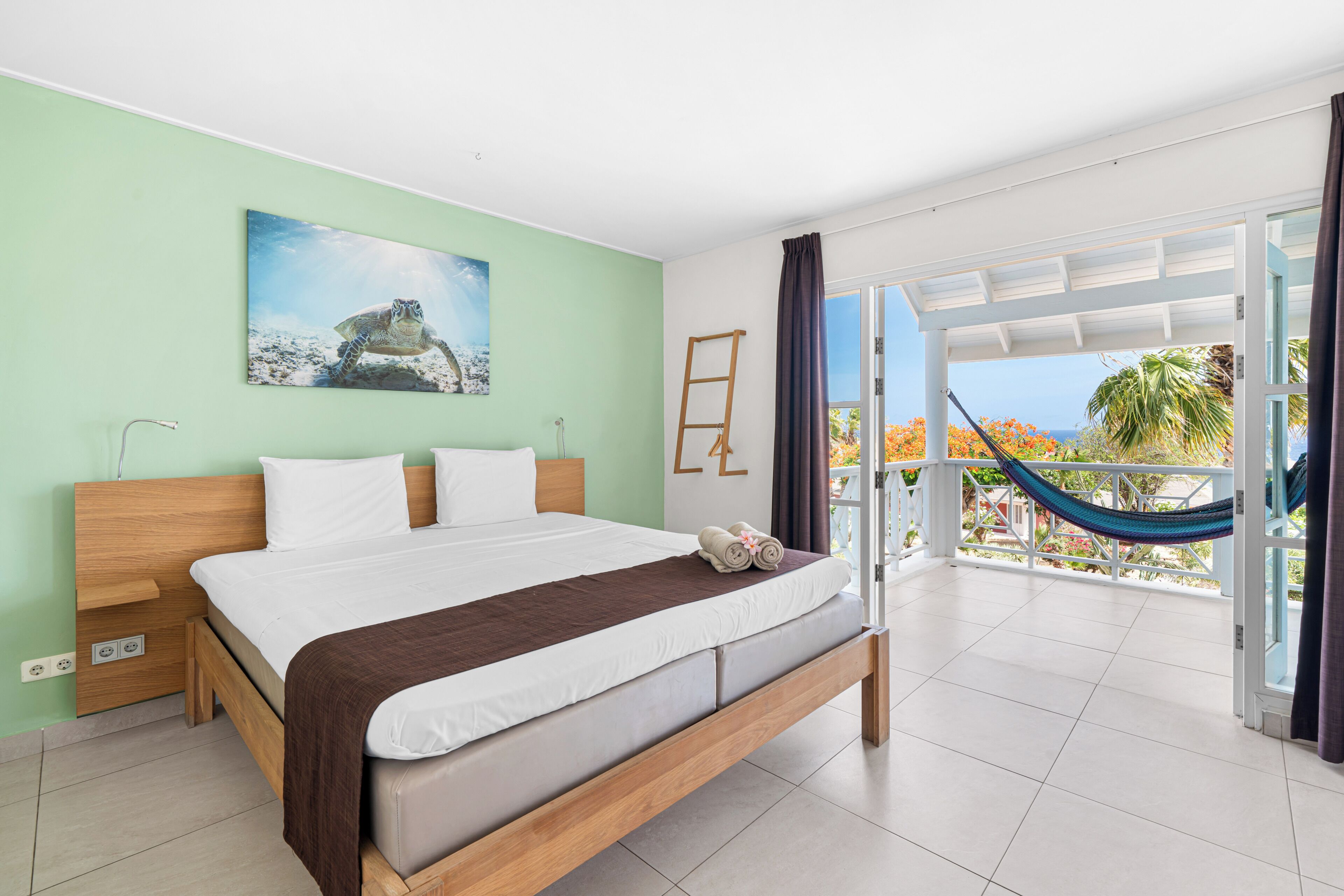 A bedroom with a bed, a painting, a hammock, and a view of the outdoors.