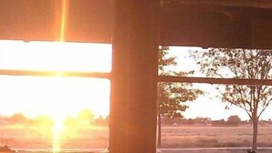 A window with a view of a sunset over a grassy field.