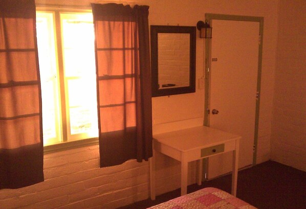 A room with a bed, a white bedside table, a mirror, and a door.