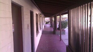 A covered corridor with doors on the left and a fence on the right.