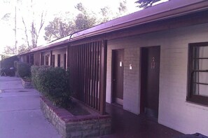 A row of motel rooms with a brick facade, numbered doors, and a small garden area.