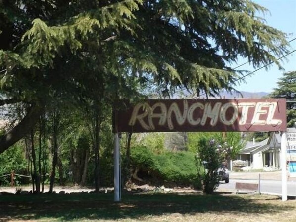 A sign for the Ranch Motel with a rustic design, surrounded by trees and a clear sky.