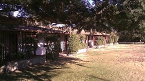 A rustic building with a porch, surrounded by trees and a grassy yard.