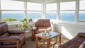 Una habitación con vista al océano, un sofá de cuero marrón, una mesa de centro de vidrio y una planta en maceta.