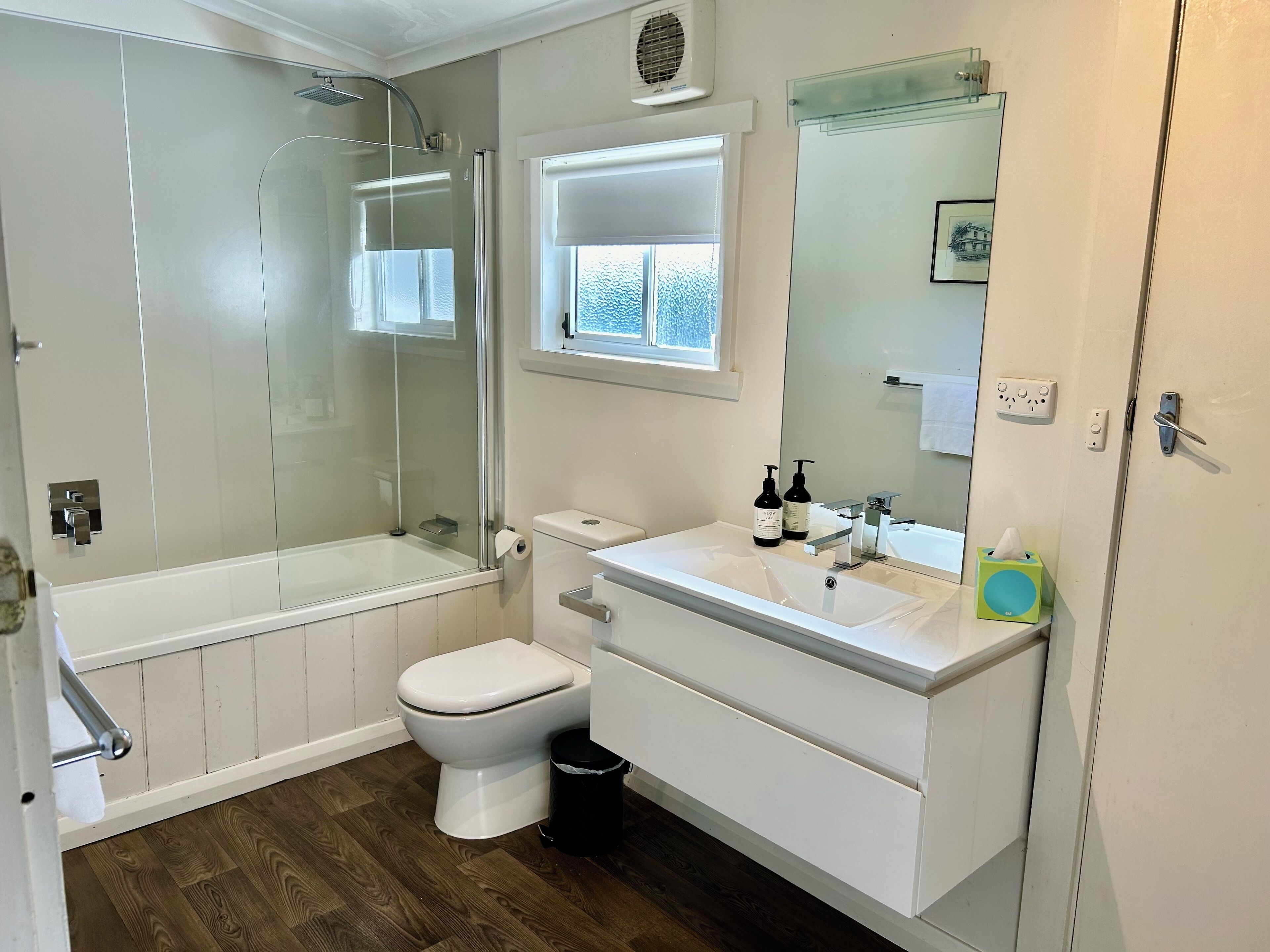 Une salle de bain moderne avec une douche à parois de verre, des toilettes et un lavabo surmonté d’un miroir.