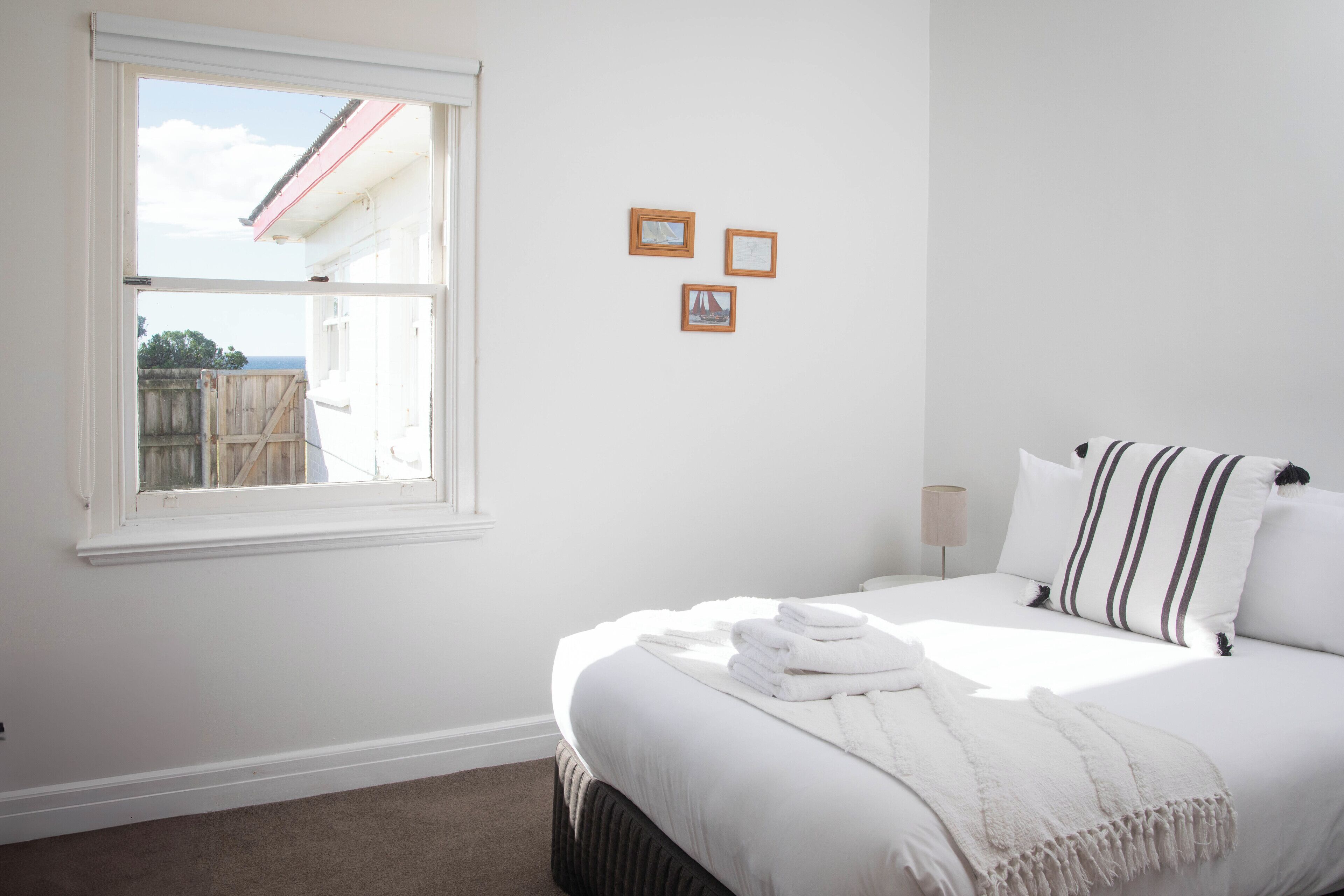 A bedroom with a large bed, a window, and three framed pictures on the wall.