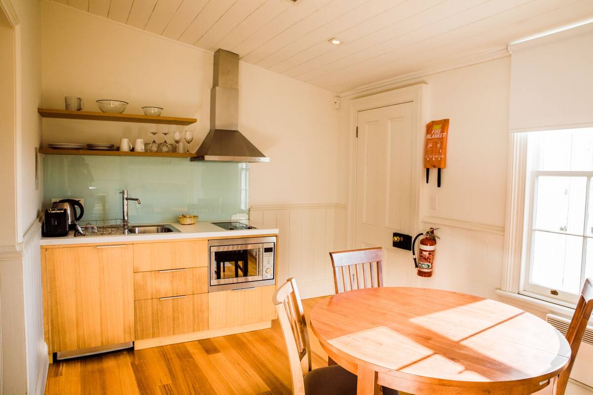 Una cocina con armarios de madera, horno empotrado, campana extractora de acero inoxidable y una mesa de comedor con sillas.