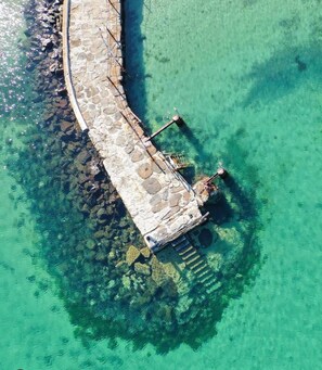 Vista aérea de un muelle de piedra que se adentra en aguas turquesas cristalinas, con escalones que bajan hasta la orilla.