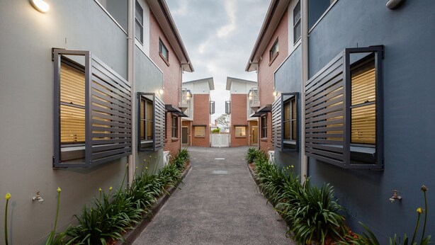 A narrow pathway flanked by buildings with external shutters, leading to a central door.