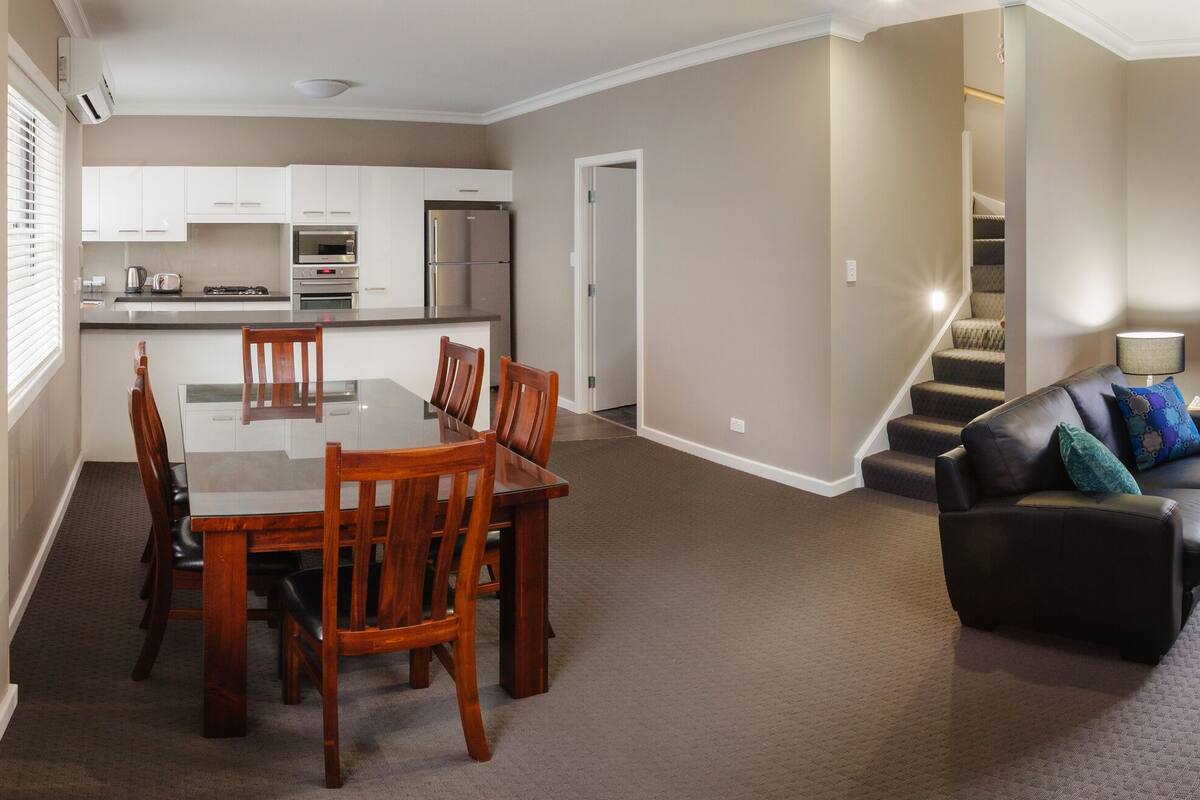 Uma sala de estar moderna com sofá, mesa de jantar com cadeiras, cozinha e televisão.