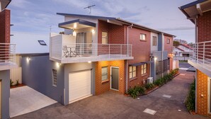 A modern two-story house with a balcony, garage, and a well-maintained garden.