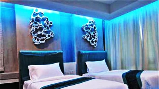 A hotel room with two beds, a dark headboard, and a wall-mounted light fixture. - Blutique Hotel (Bangkok)