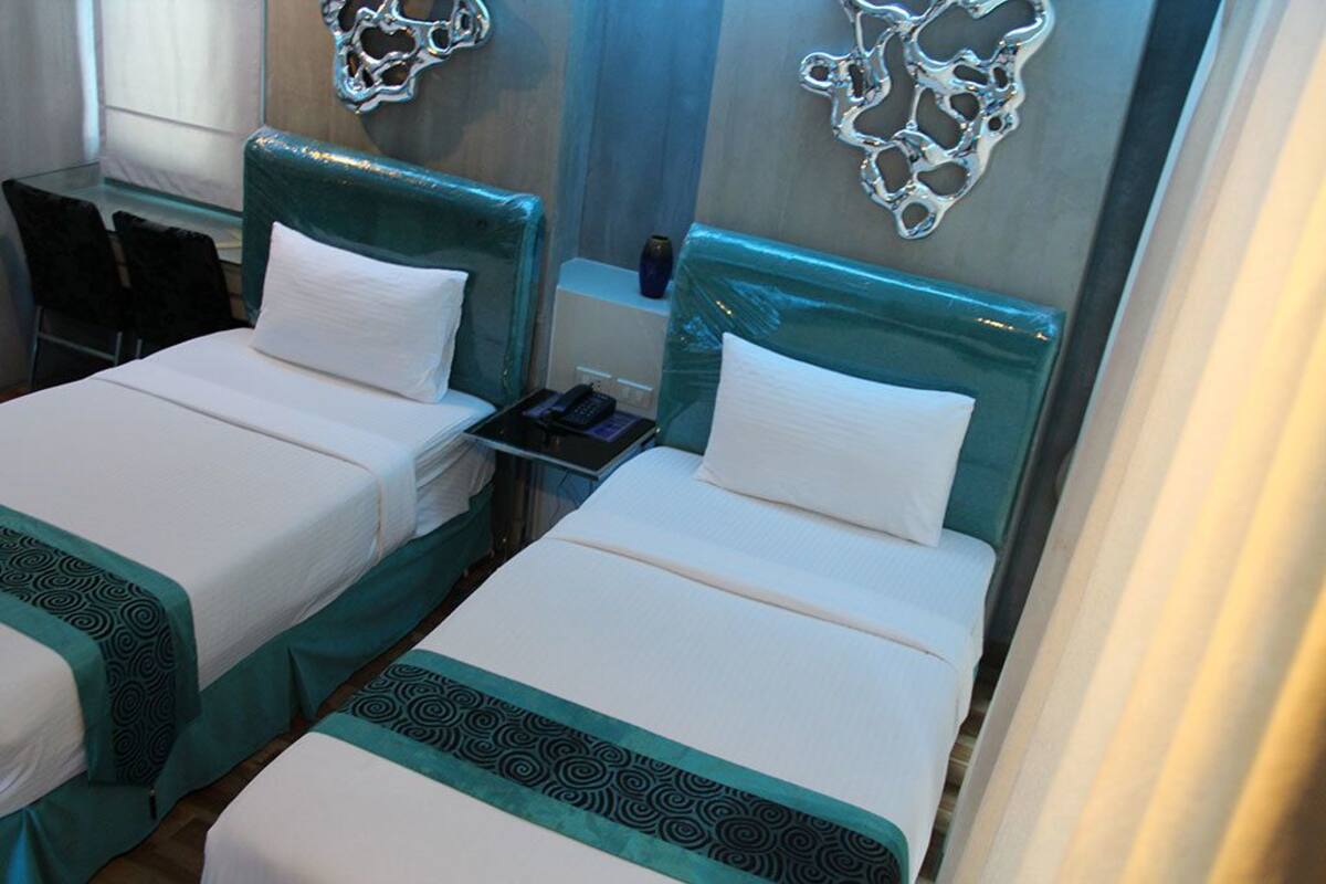 Two twin beds with teal headboards and white bedding, a bedside table with a phone, and a decorative wall piece.