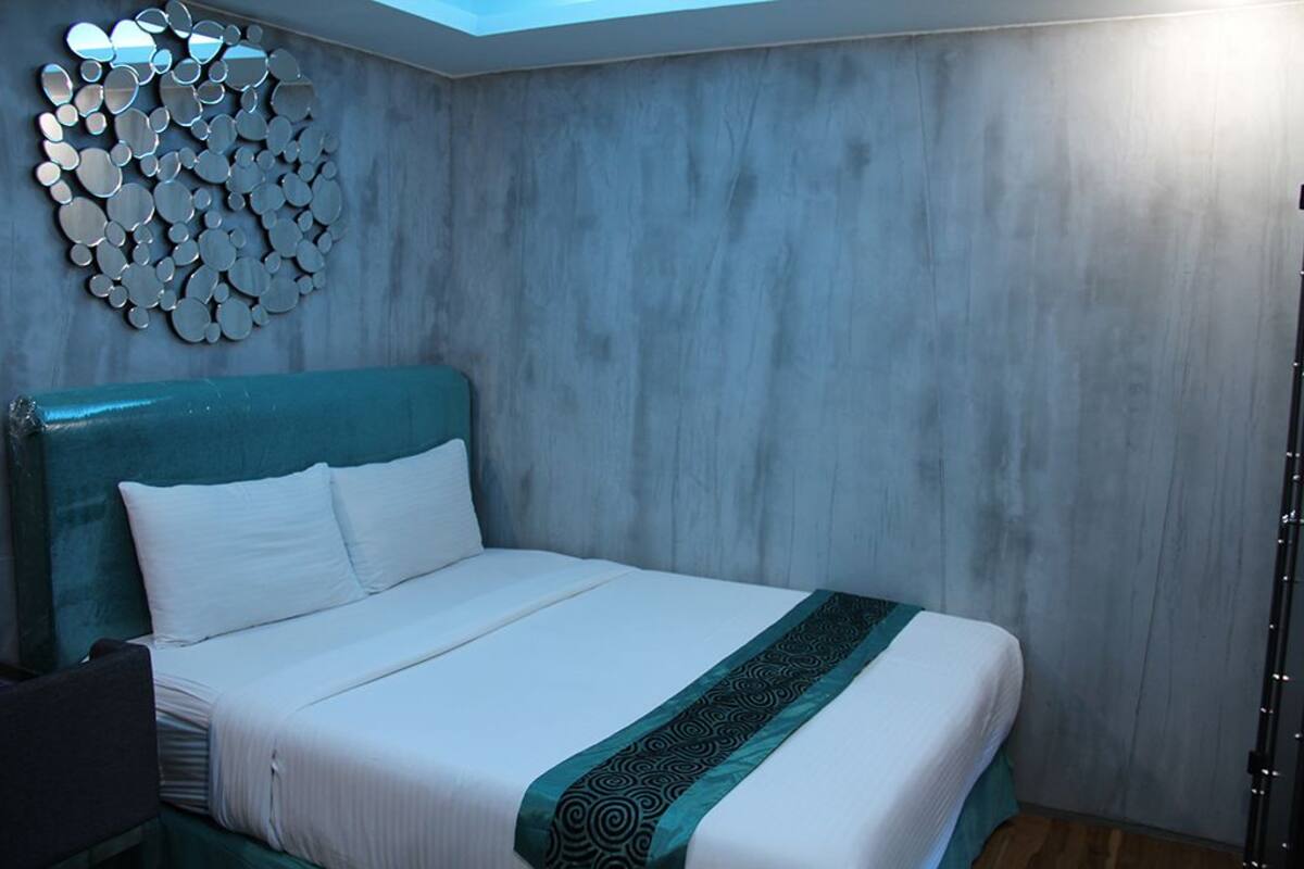 A hotel room with a bed, a headboard, a wall with a circular mirror design, and a skylight.