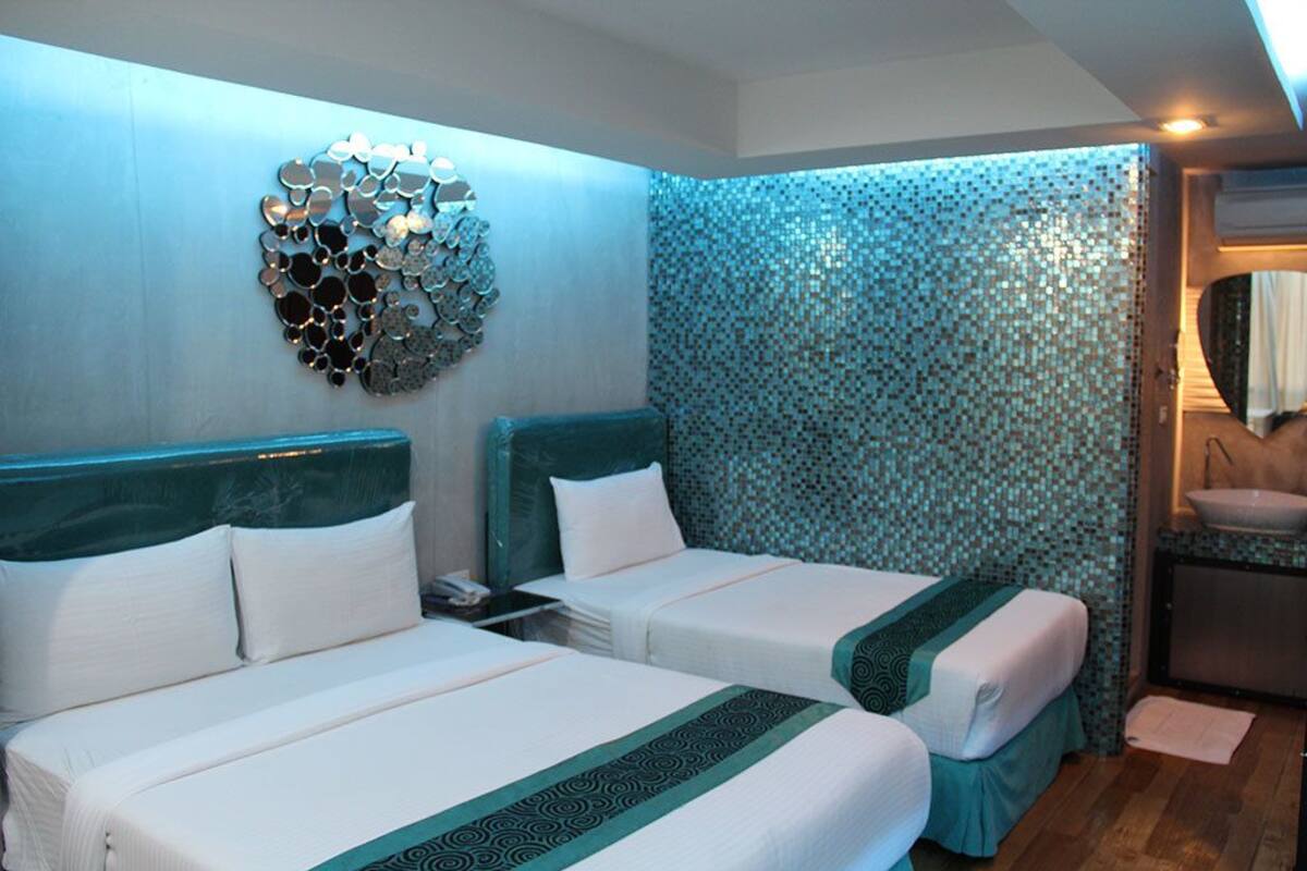 A hotel room with two beds, a decorative wall art piece, a bathroom with a sink, and a patterned wall.