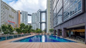 Una piscina en la azotea con sillas de descanso y una zona de restaurante, rodeada de edificios altos.