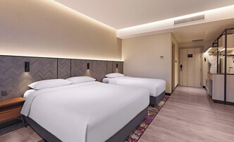 A hotel room with two beds, a wooden headboard, a bench, a small table, and a walk-in closet.