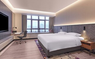 A modern hotel room with a large bed, a desk, a chair, a TV, and a window with curtains.